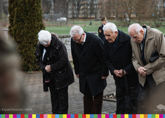 Czterech starszych mężczyzn pochyla głowy przed pomnikiem.