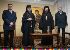 Dwie osoby duchowne oraz dwóch samorządowców stoją przy stole, na którym znajdują się trzy lampiony