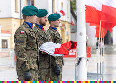 trzech żołnierzy stojących przy maszcie, jeden z nich trzema flagę
