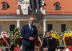 Dwóch mężczyzn pozuje do zdjęcia. W tle pomnik Marszałka Piłsudskiego