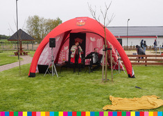 Czerwony namiot z herbem Korycina. Pod namiotem zespół muzyczny.