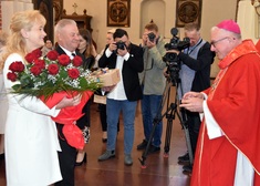 Kobieta z kwiatami i mężczyzna z podarkiem stoją przed biskupem