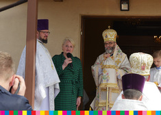 Wiesława Burnos z mikrofonem stoi pomiędzy duchownymi Cerkwi