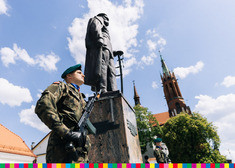 Żołnierz stoi pod pomnikiem Józefa Piłsudskiego. W tle widać budynek katedry.