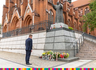 Marek Malinowski stoi na baczność przed pomnikiem, pod którym leżą wieńce
