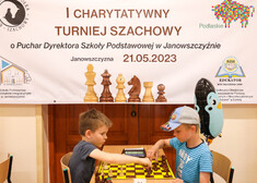dzieci grają w szachy, za nimi znajduje się banner reklamujący wydarzenie