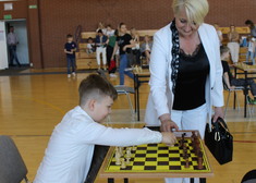 Chłopiec podczas gry w szachy, obok stoi kobieta