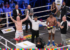 Sędzia podnosi do góry rękę boksera. który znajduje się na zdjęciu po lewej stronie