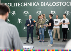 Pod ścianą z logotypem Politechniki Białostockiej stoi sześć osób
