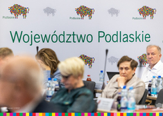 Osoby siedzące, w tle ścianka z napisem Województwo Podlaskie i logiem Podlaskie.eu
