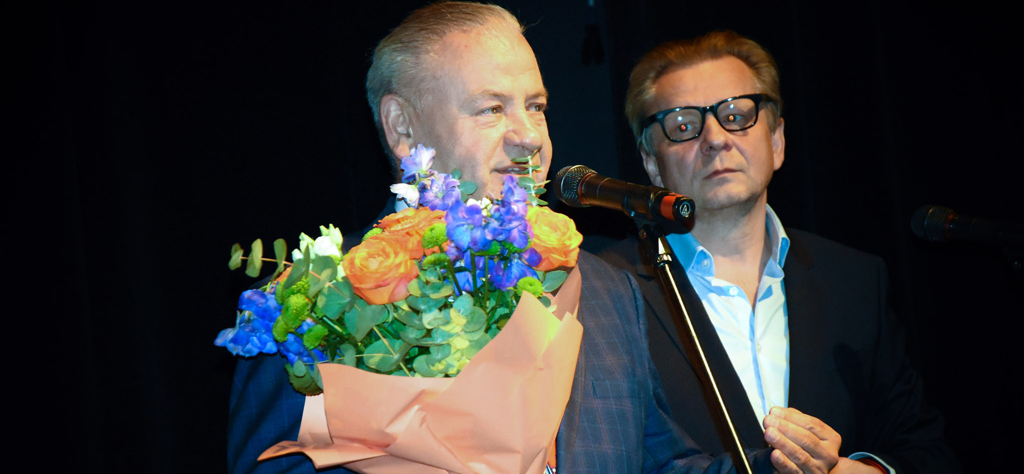 Wicemarszałek Marek Olbryś trzyma bukiet z kwiatami i przemawia przez mikrofon
