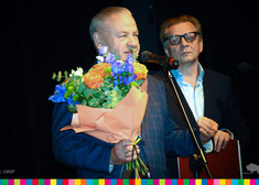 Wicemarszałek Marek Olbryś trzyma w dłoni bukiet pełny kolorowych kwiatów. Za jego stoi mężczyzna
