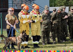 Grupa stojących osób, część w mundurach, obok jednej stoi pies