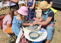 Dziewczynka robi naczynie z gliny na kole garncarskim przy pomocy dorosłych