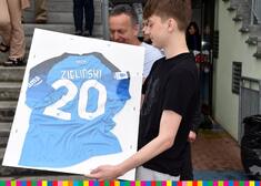 Chłopiec trzyma koszulkę sportową z nazwiskiem Zieliński i z numerem 20