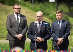 Marszałek Artur Kosicki mówi przez mikrofon pomiędzy dwoma mężczyznami