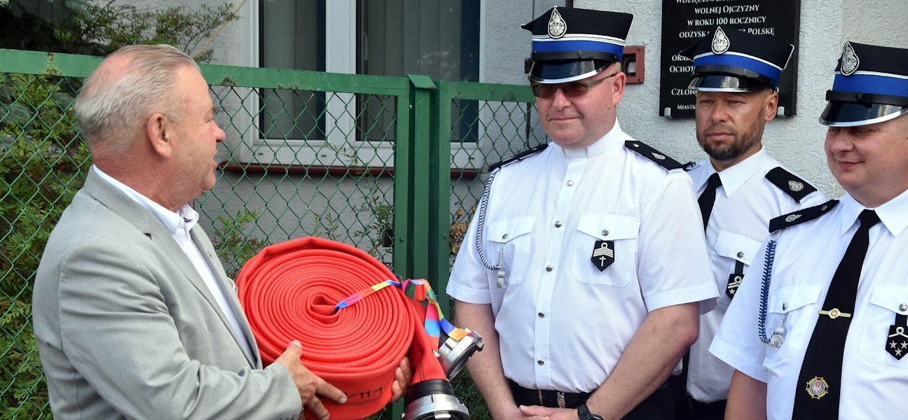 Mężczyzna przekazuje strażakom ochotnikom zwiniętego węża strażackiego