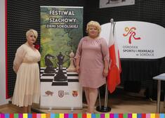 Wiesława Burnos, członek zarządu i Ewa Kulikowska, burmistrz Sokółki stoją przy fladze biało-czerwonej i banerze festiwalu