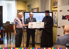 Marszałek Artur Kosicki przekazuje czek prawosławnemu mnichowi. Po lewej stoi starszy mężczyzna