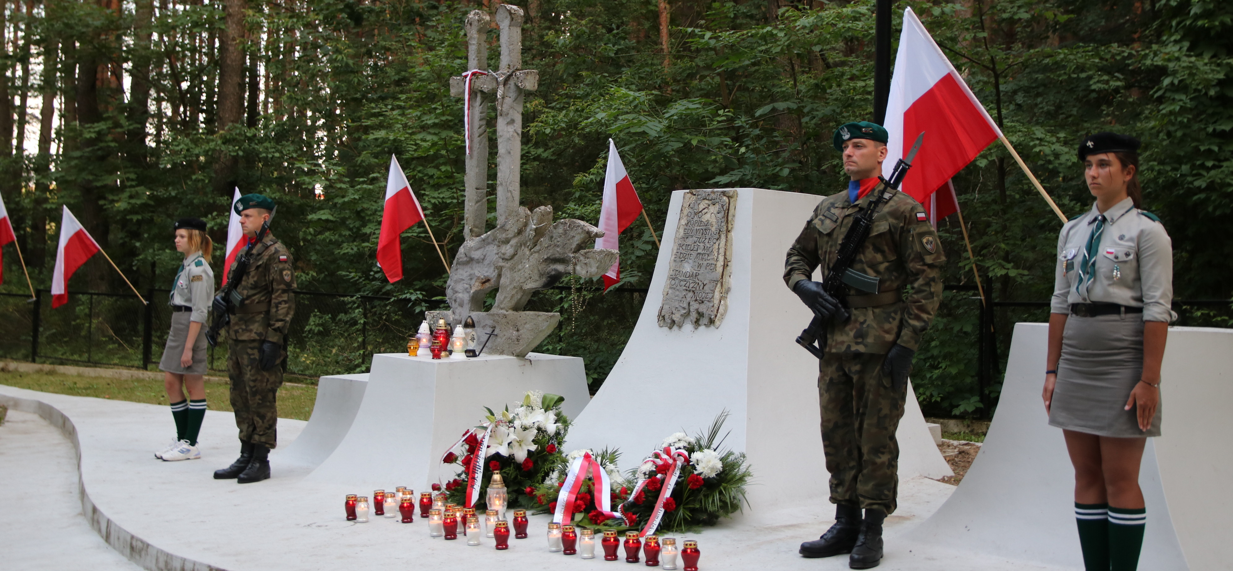 Dwóch żołnierzy i dwie harcerki stojący na baczność przy pomniku