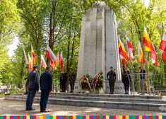 Cywil i mundurowy stoją przed pomnikiem przy którym stoi asysta honorowa