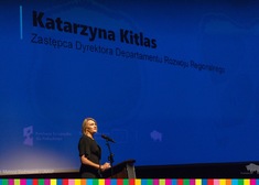 Stojąca kobieta na tle ekranu z napisem Katarzyna Kitlas