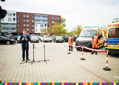 Marek Malinowski, członek zarządu przemawia na tle ambulansów i samochodów na parkingu