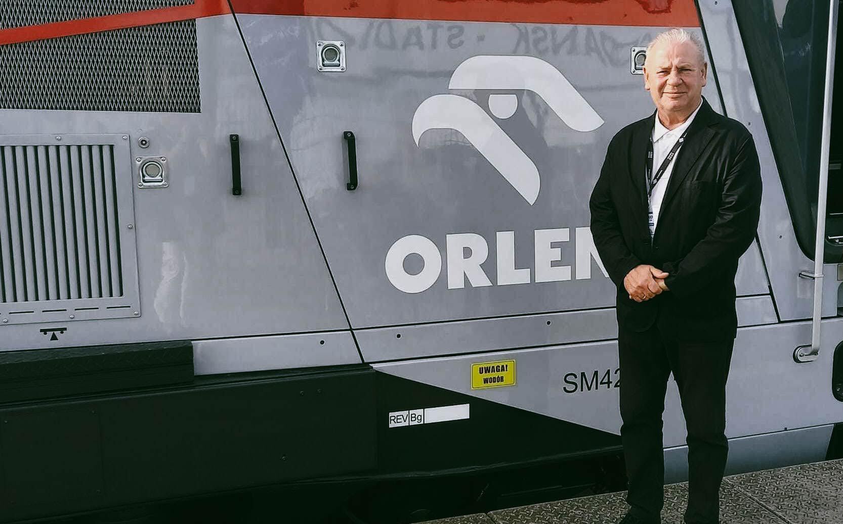 Wicemarszałek Marek Olbryś stoi na tle lokomotywy z logotypem Orlenu