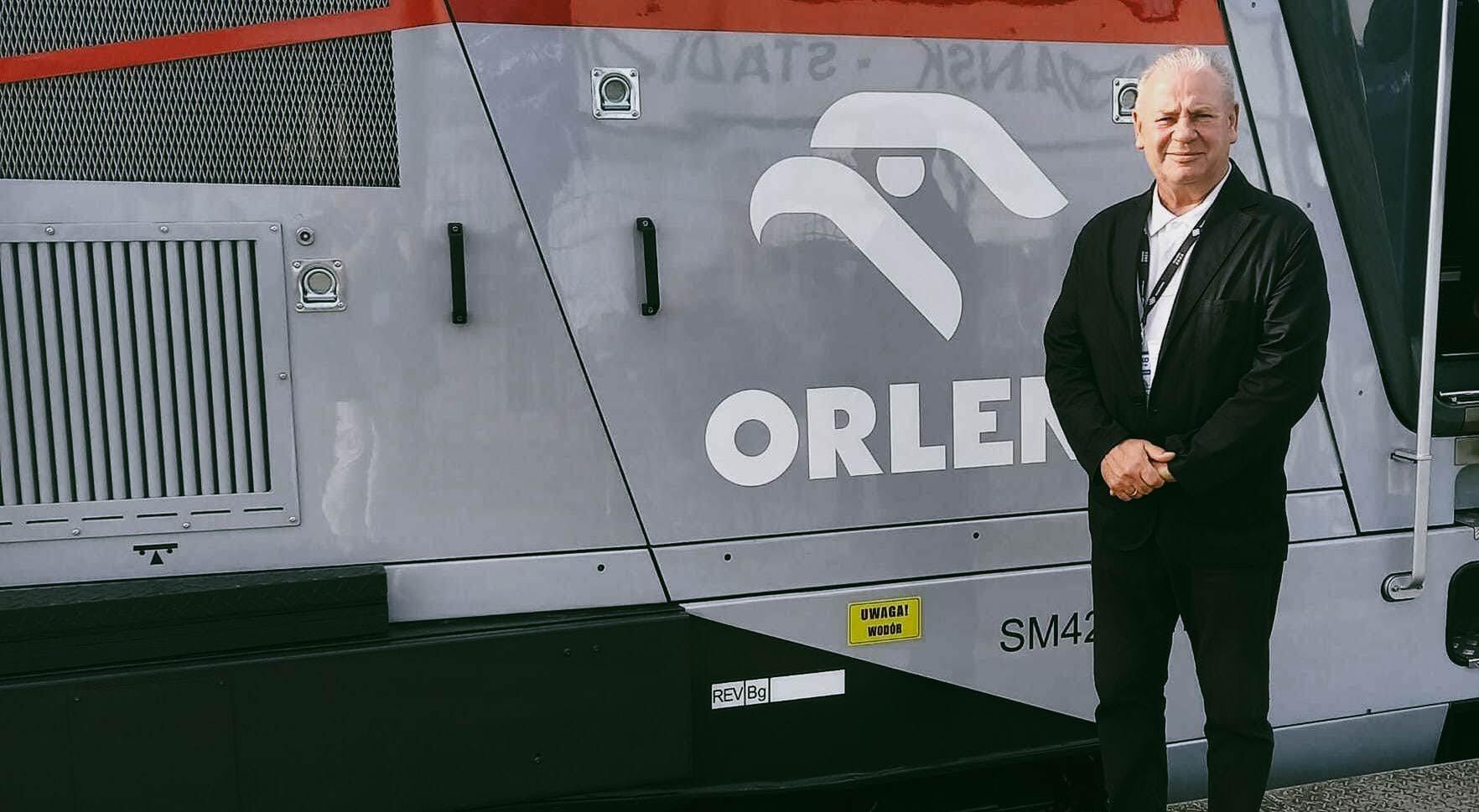 Wicemarszałek Marek Olbryś stoi na tle lokomotywy z logotypem Orlenu
