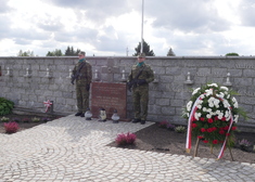Dwóch żołnierzy stojących przy marmurowej tablicy pamięci na cmentarzu