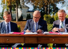 Trzech mężczyzn siedzi przy stole i podpisuje umowy