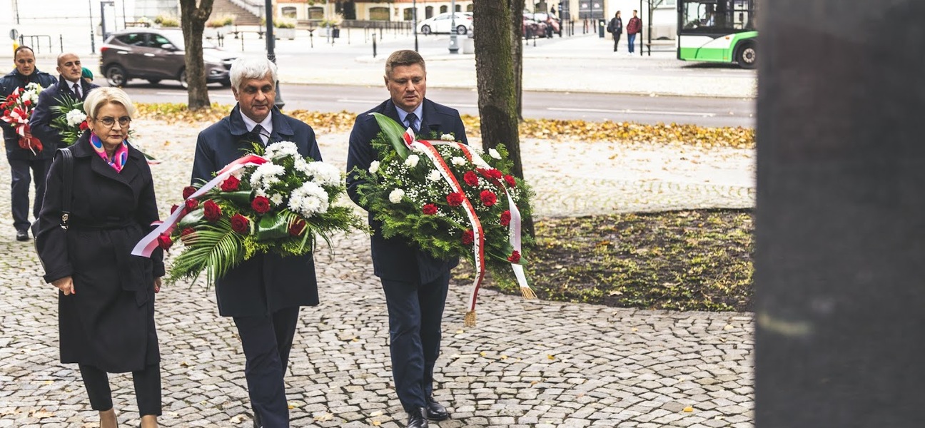 Oficjele niosą wiązanki z biało czerwonymi wstęgami, w tle jest Katedra Białostocka