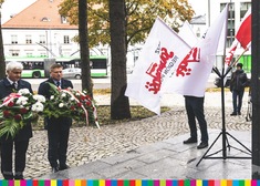 Dwaj mężczyźni przy pomniku, obok flagi z napisem 