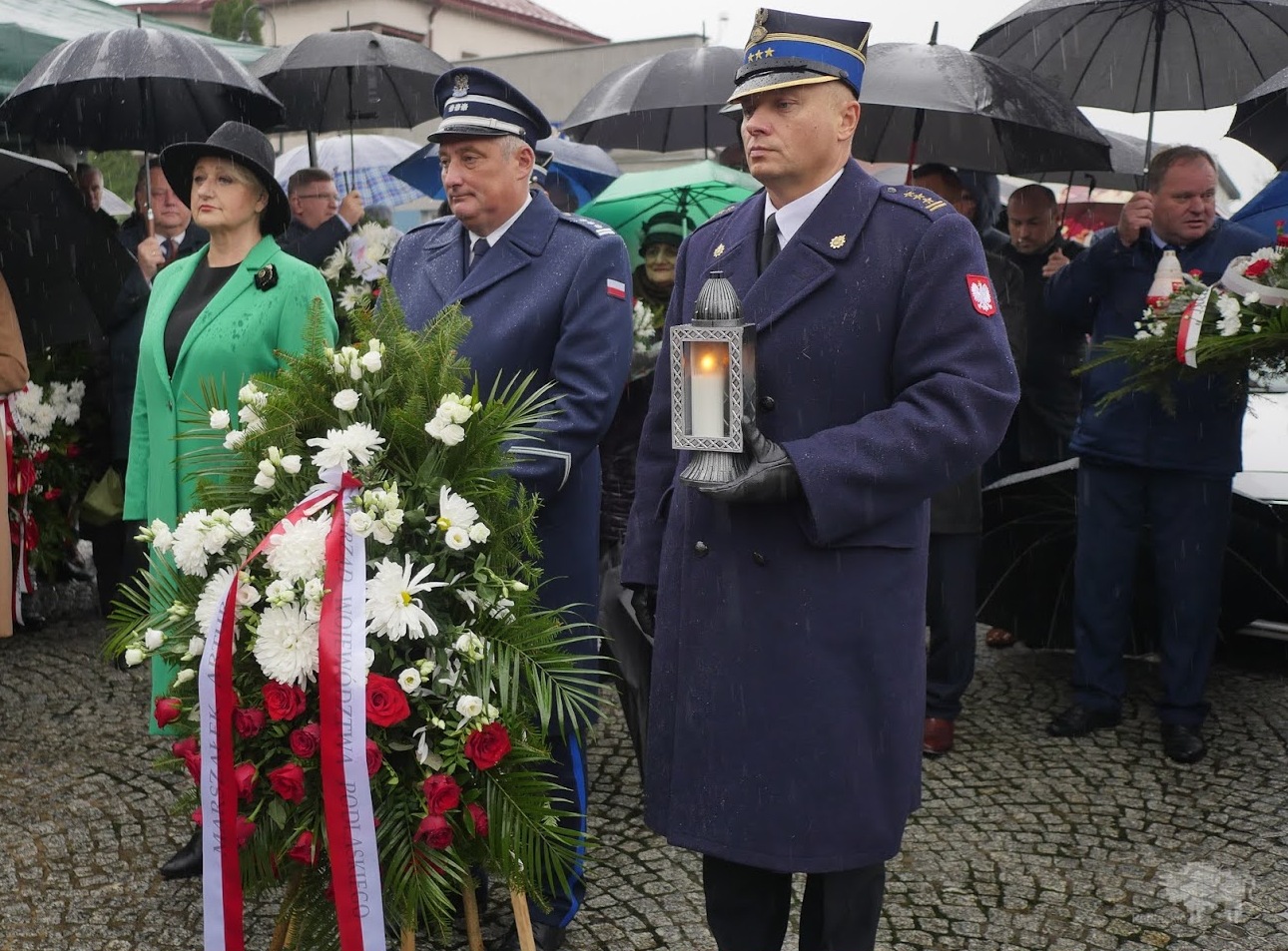 Wiesława Burnos, członek zarządu województwa oraz mężczyźni w mundurach oddają hołd pod pomnikiem, jeden z mężczyzn trzyma wiązankę kwiatów, drugi lampion