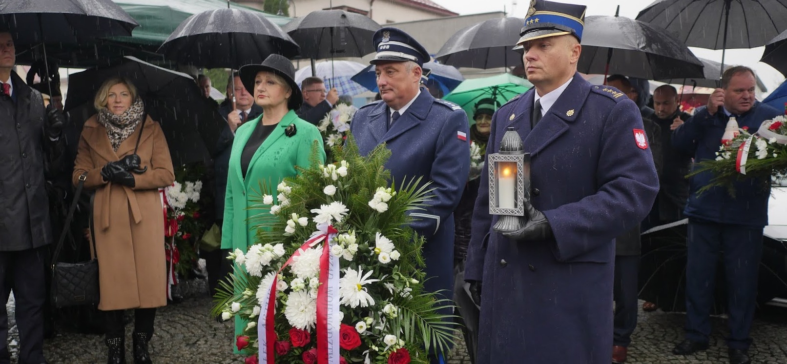 Wiesława Burnos, członek zarządu województwa oraz mężczyźni w mundurach oddają hołd pod pomnikiem, jeden z mężczyzn trzyma wiązankę kwiatów, drugi lampion