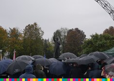 Uczestnicy uroczystości schowani pod parasolami, w tle widać pomnik bł. ks. Jerzego Popiełuszki