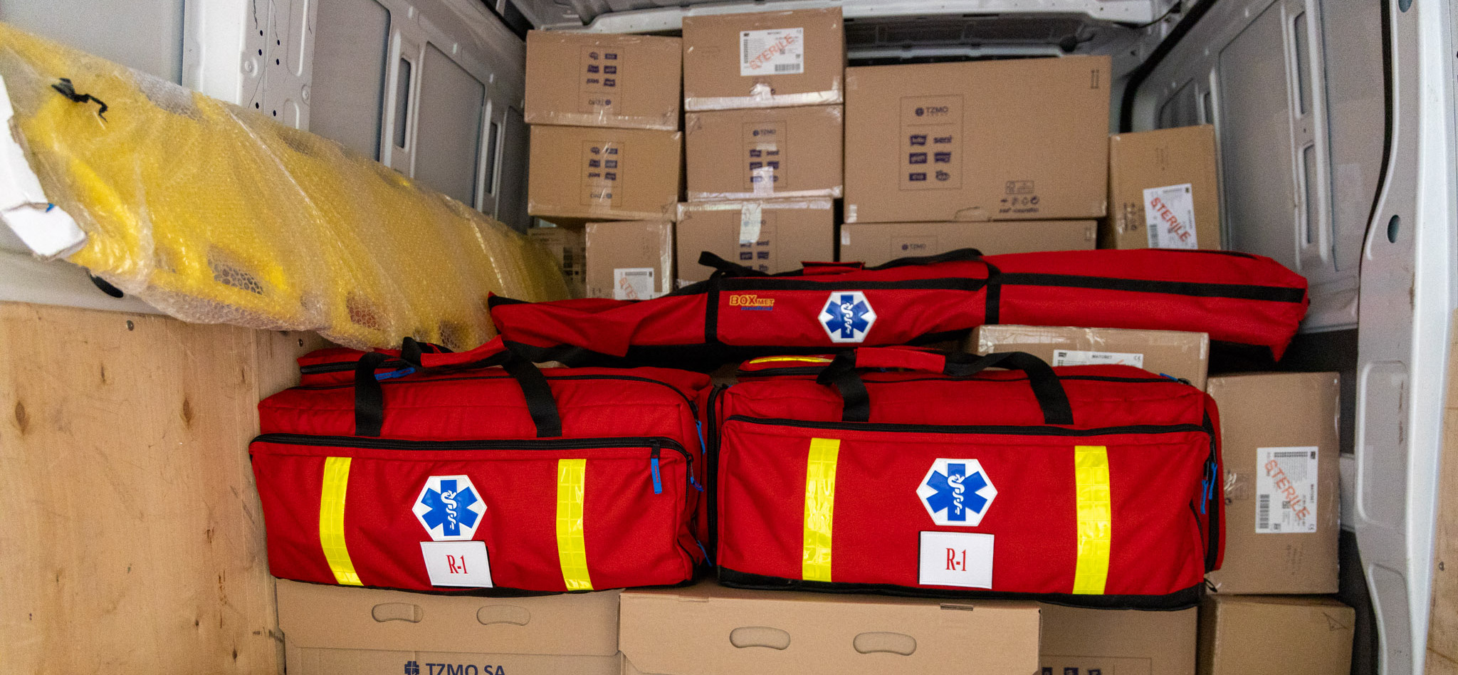 Czerwone torby medyczne i pudełka kartonowe znajdujące się w białym busie.