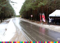 Nowa jezdnia, po obu stronach las, po prawej stronie widoczne flagi Polski 