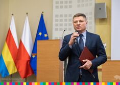 Marek Malinowski przemawia w tle stoją flagi Polska i europejska