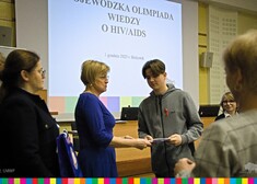 Dwie kobiety wręczają dyplom i nagrodę chłopakowi, w tle widać rzutnik z napisem: Wojewódzka Olimpiada Wiedzy o HIV/AIDS