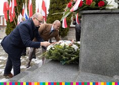 Mężczyźni składają kwiaty pod pomnikiem