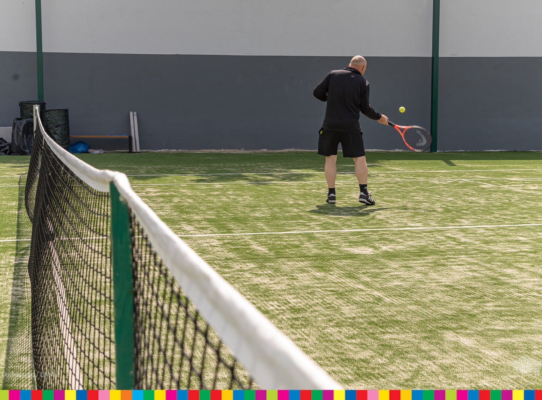 Zielony kort tenisowy, na którym tenisista odbija piłkę tenisową.