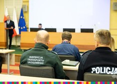Uczestnicy wydarzenia siedzą na auli, w tle widać mężczyznę stojącego przy mównicy oraz mężczyznę siedzącego przy komputerze 