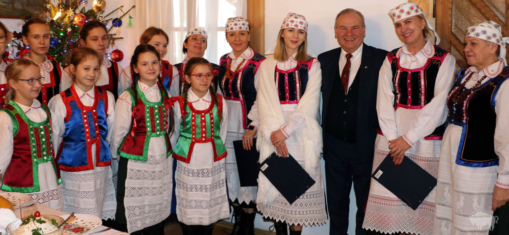 Wicemarszałek Marek Olbryś z kobietami i dziećmi w strojach ludowych, po lewej stronie choinka