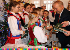 Wicemarszałek Marek Olbryś wręcza dzieciom w strojach ludowych bombkę i pocztówki świąteczne, w tle widać choinkę