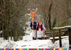 Kobieta i mężczyzna w strojach ludowych idą zaśnieżonym lasem, niosą kolorową gwiazdę 