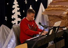 Mężczyzna w świątecznym sweterku grający na elektrycznym pianinie