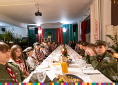 siedzący młodzi harcerze w mundurach przy wigilijnym stole 
