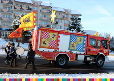 Przyozdobiony wóz strażacki za którym podąża orkiestra orszaku