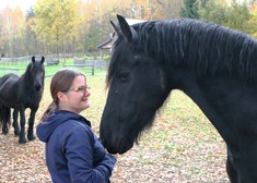 Pani Karina stoi przy czarnym koniu, w tle drugi czarny koń.